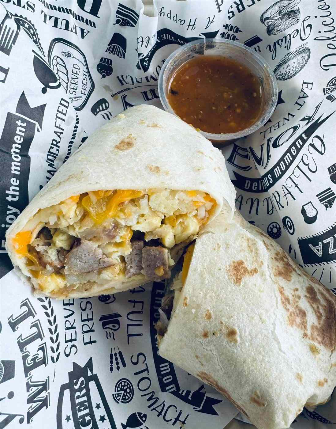A breakfast burrito cut in half with a cup of salsa