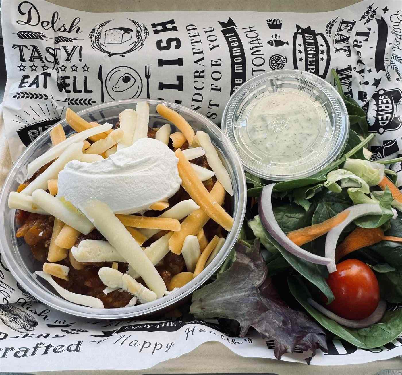 A chili bowl with cheese and sour cream, and a side salad with ranch