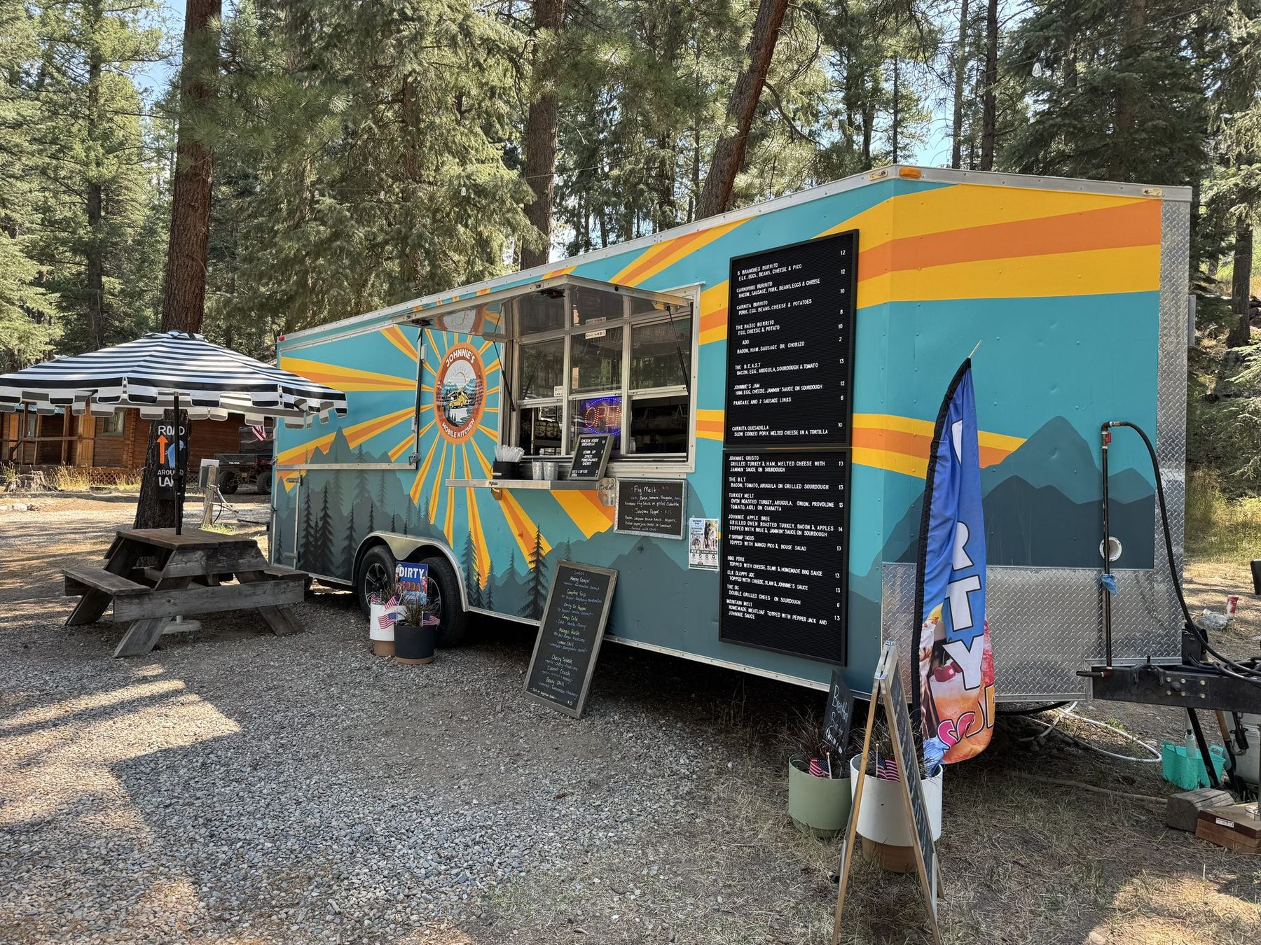 The trailer pitched under the pines with the menu boards up and the window open